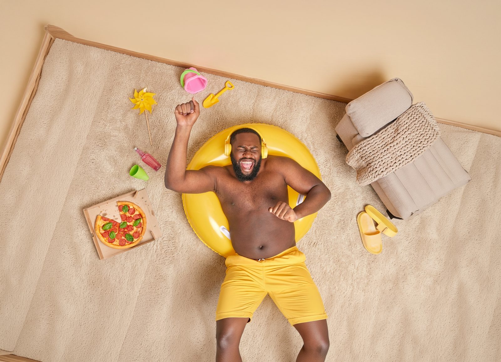 A man in swim shorts and headphones lounging on a rubber ring on his living room rug, warm as a summer holiday at home